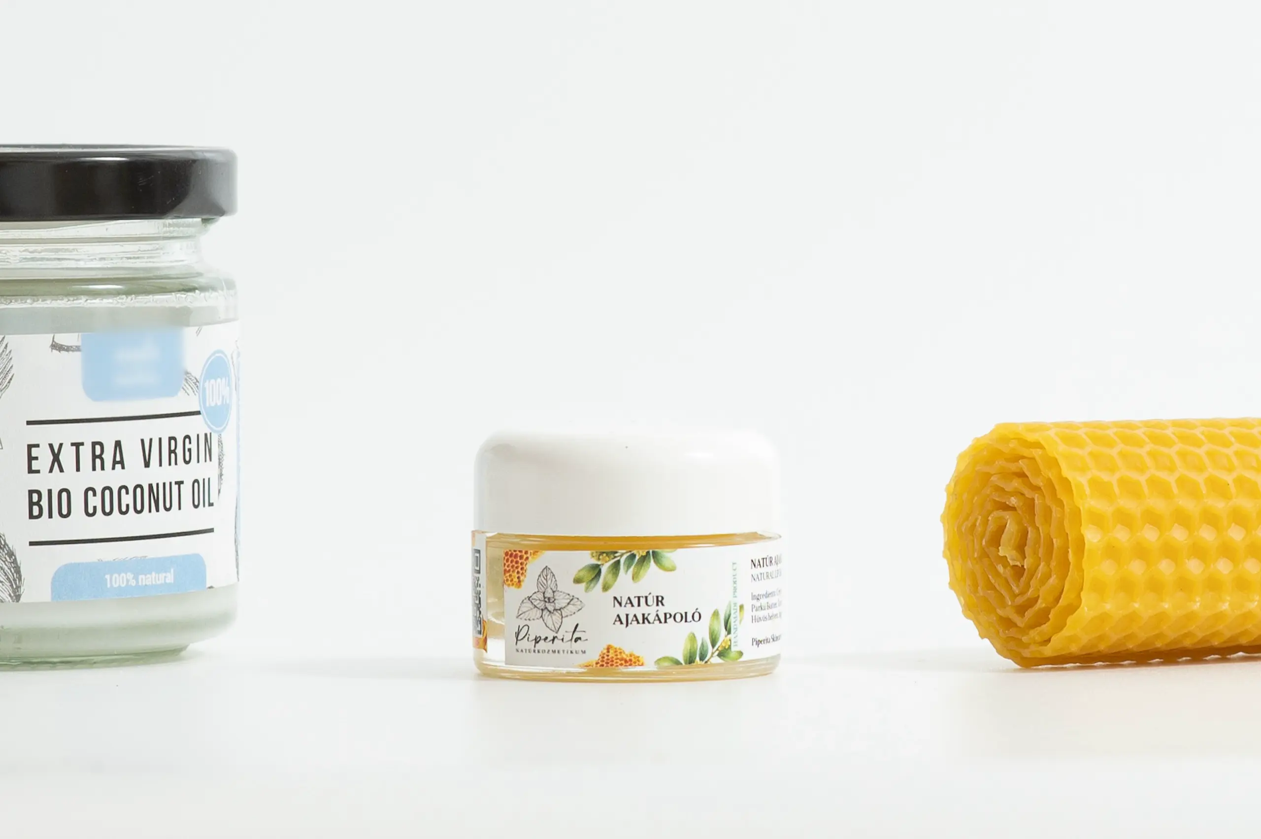 Natúr ajakápoló üveg tégelyben, mellette kókuszolaj és méhviasz természetes háttéren