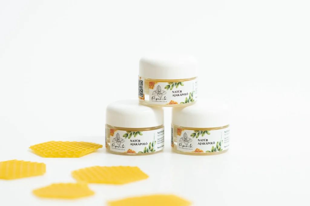 Natúr ajakápoló tégelyek egymásra helyezve, méhviasz darabokkal világos háttéren