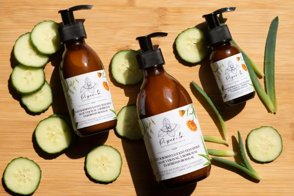 Piperita natúr bőrnyugtató testápolók uborkaszeletekkel és aloe vera levelekkel fa alapon, napfényes nyári hangulatban.
